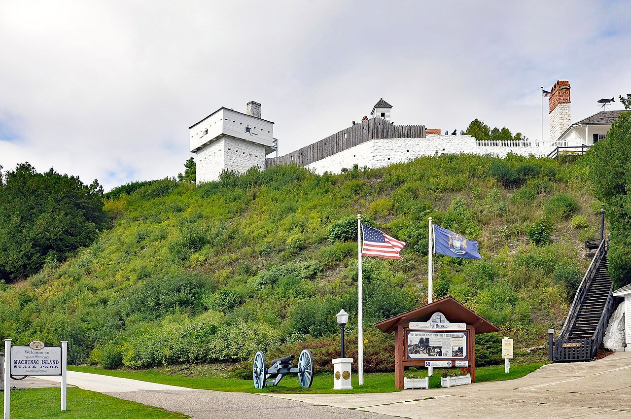 White historic fort buildings and a cannon above a green slope on Mackinac Island, Michigan.